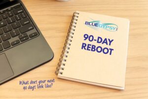A spiral notebook labeled Blue Gypsy 90-Day Reboot sits on a wooden desk next to a laptop keyboard, with the handwritten question: What does your next 90 days look like?